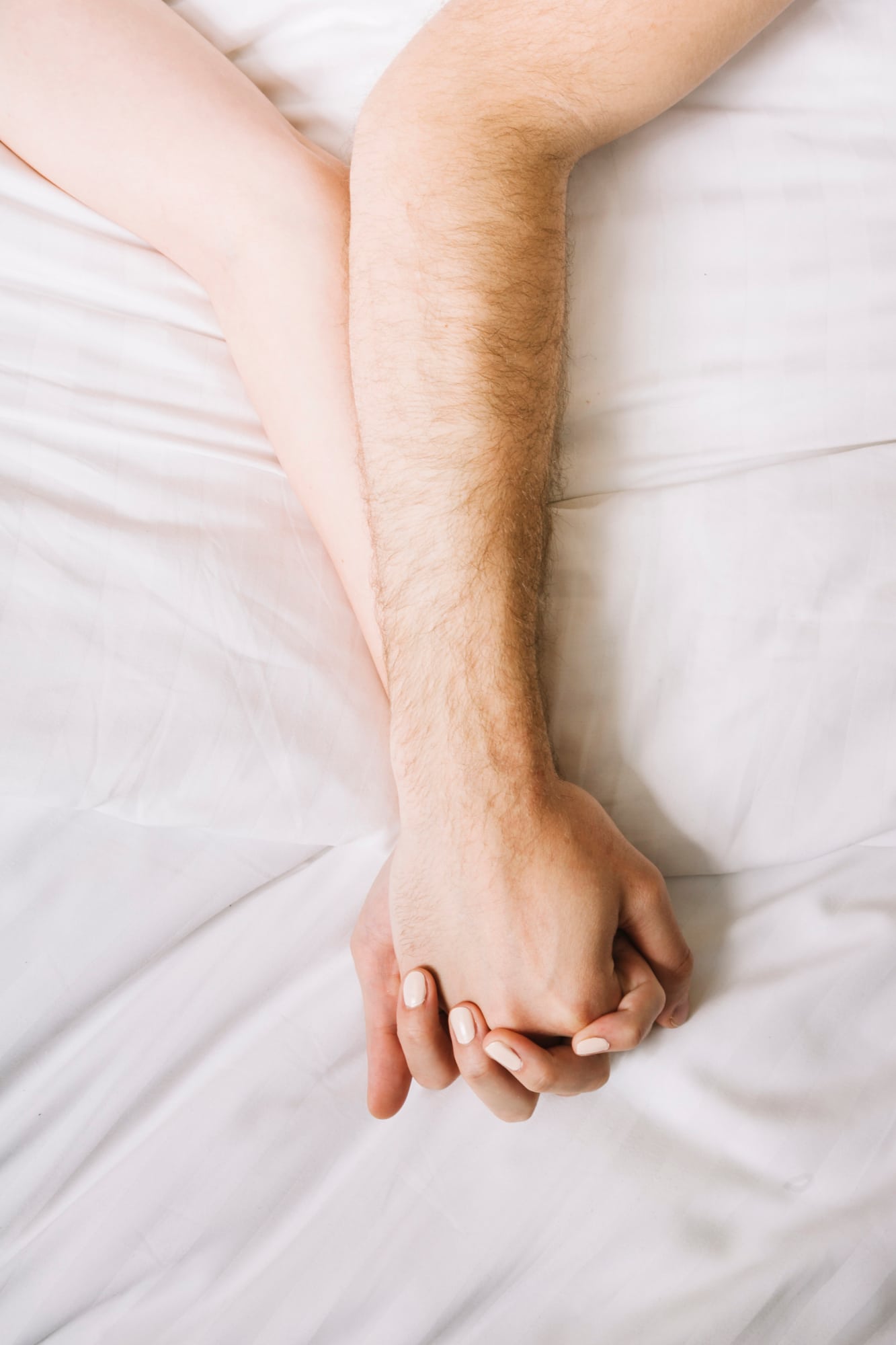Deux personnes allongées côte à côte se tenant la main, illustrant la complicité, l'intimité et le désir au sein du couple.