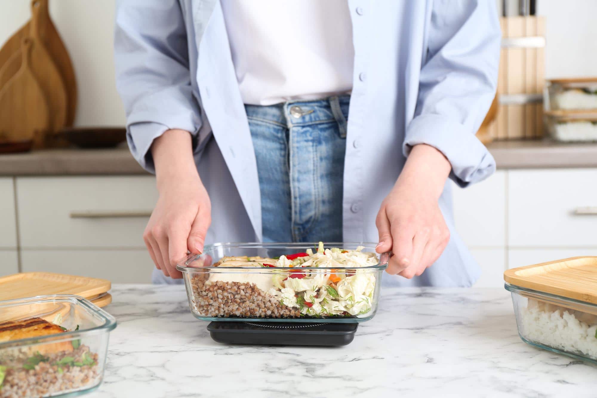 Préparation d'un repas de batch cooking dans une boîte alimentaire en verre avec céréales, légumes et protéines, pour organiser les repas de la semaine.