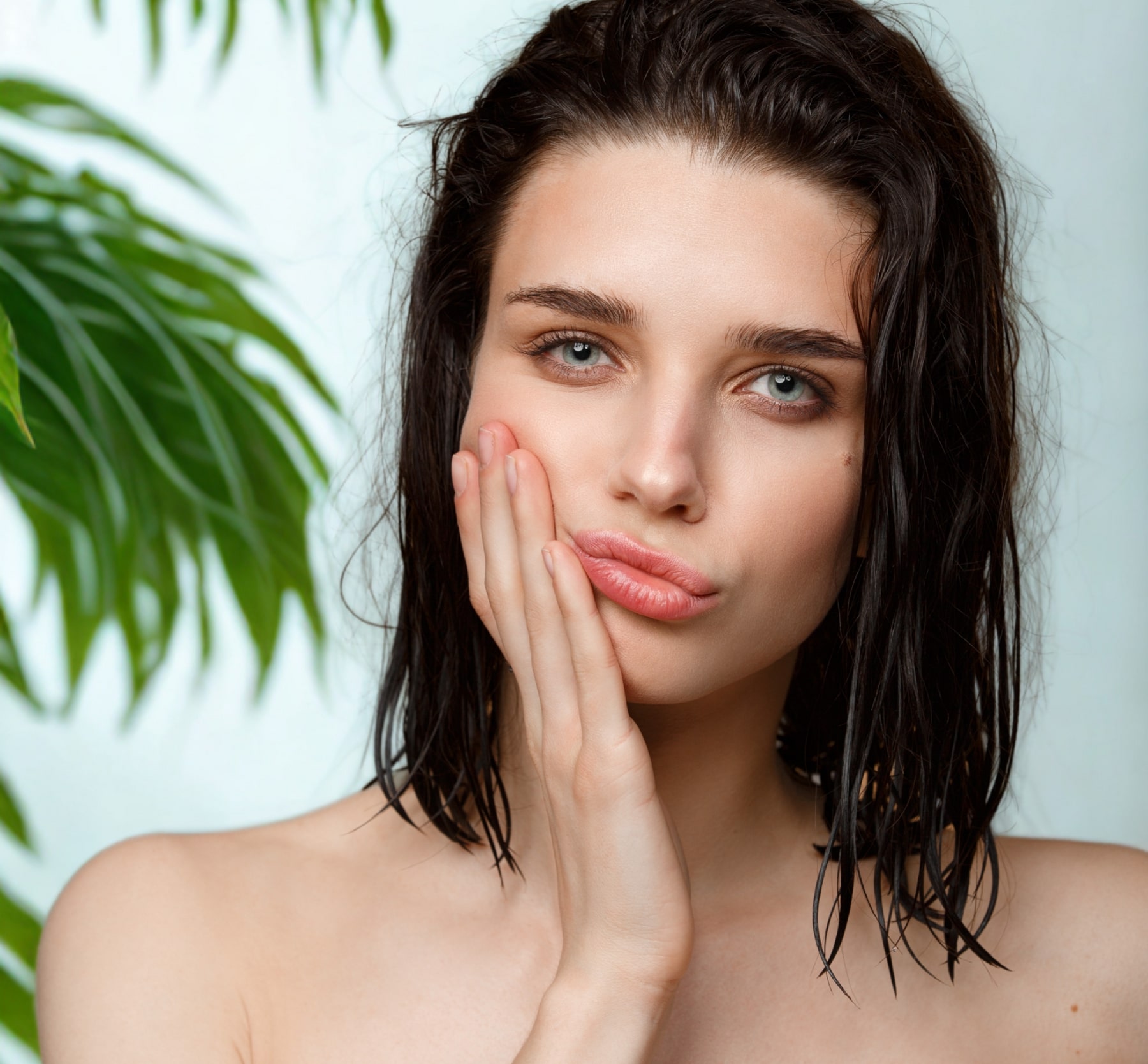Jeune femme au teint frais posant avec une expression pensive, entourée de feuilles vertes sur fond clair – symbole de beauté naturelle et ayurvédique.