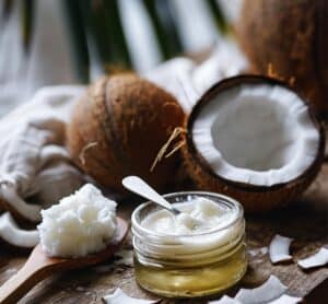 Huile de coco bio dans un petit pot en verre, accompagnée de copeaux de coco frais et d’une cuillère en bois, sur fond naturel en bois brut.