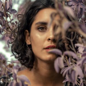 Portrait d’une jeune femme au milieu des plantes, entourée de verdure, dans une ambiance douce et naturelle. Un clin d’œil à la beauté ayurvédique, en harmonie avec la nature.