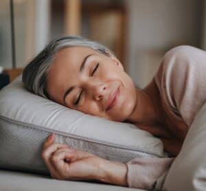 Femme détendue souriante dormant paisiblement sur un oreiller confortable, illustrant un sommeil naturel et réparateur.