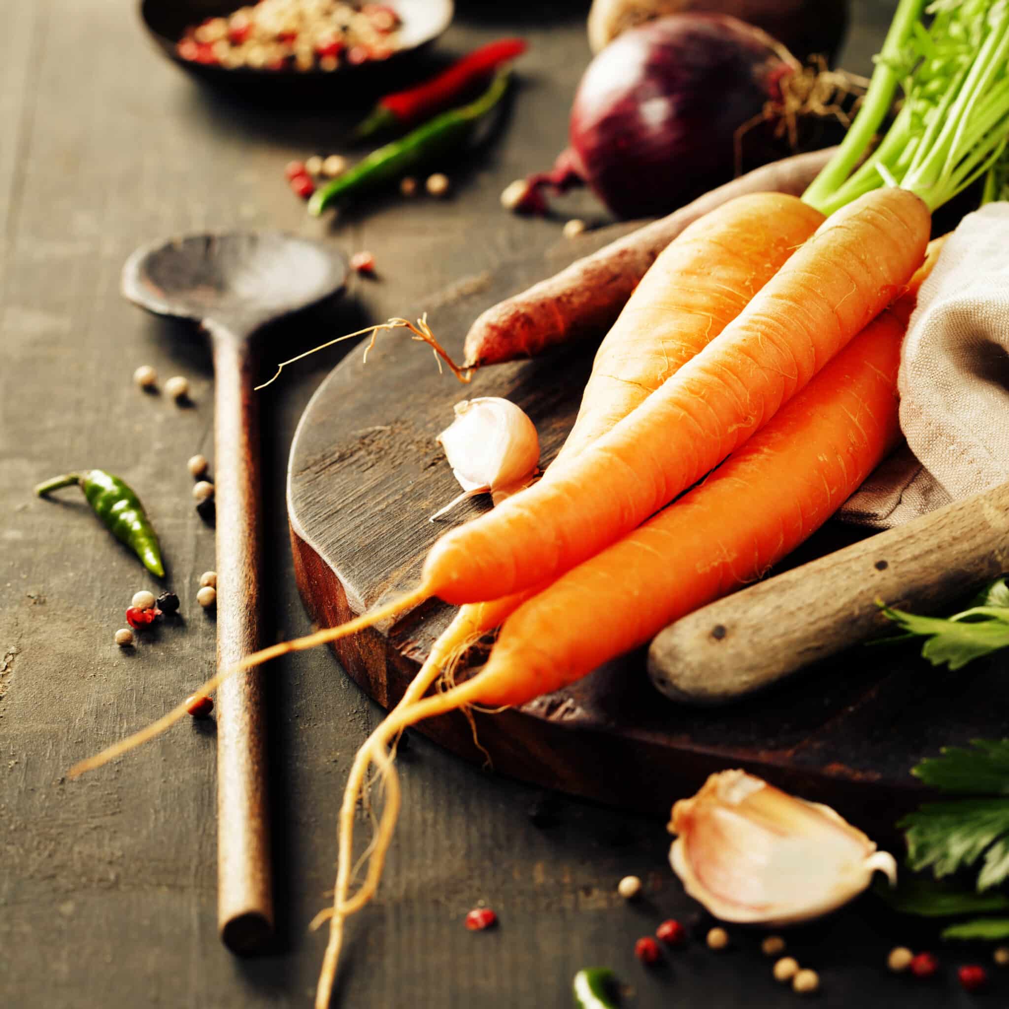 Carottes posées sur une planche en bois avec épices, ail et légumes, ambiance cuisine