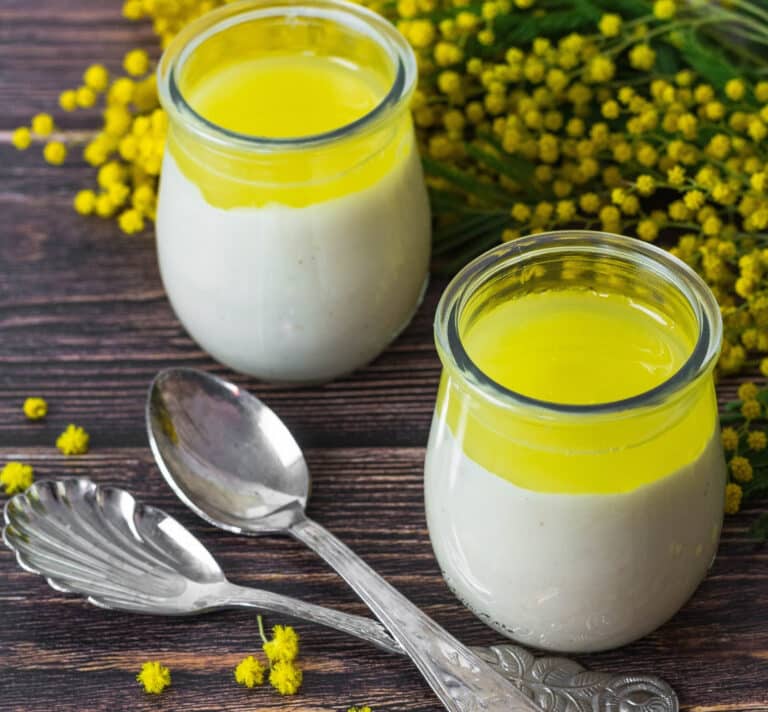 Petits pots de crème végétale à l’amande surmontés d’un curd citron cédrat, avec des cuillères sur une table en bois.