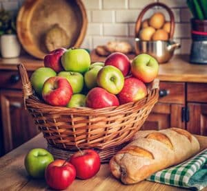 Panier de pommes et pain sur une table de cuisine, symbolisant les aliments du quotidien et la consommation consciente
