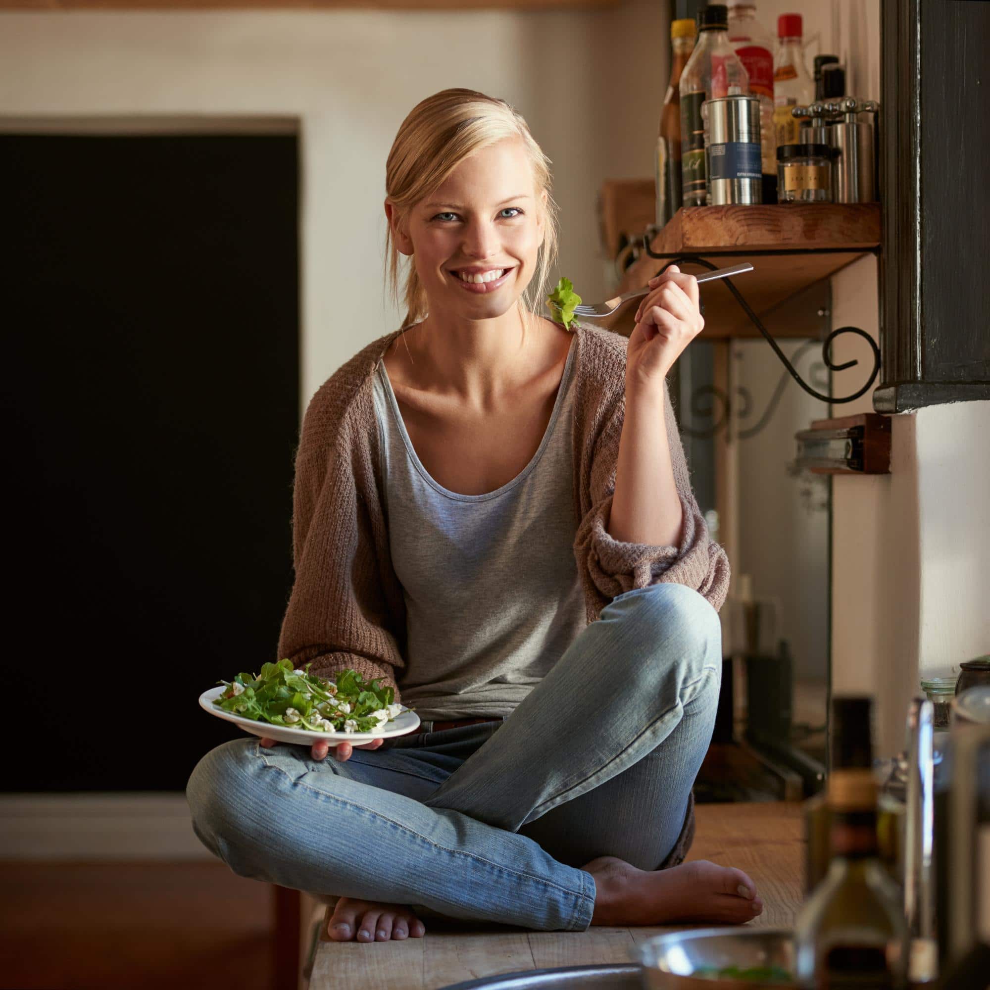 Jeune femme dégustant une salade dans une cuisine chaleureuse, illustration d’une alimentation végétale simple et naturelle