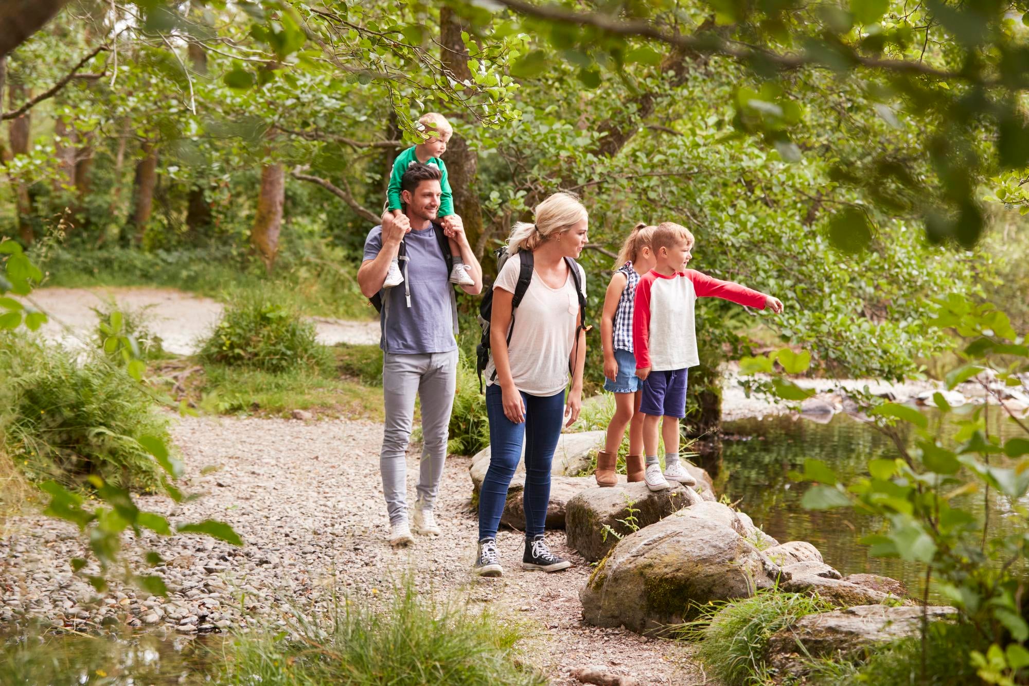 Papa et sa famille en promenade au bord d'une rivière, partageant un moment de découverte et de complicité en pleine nature.