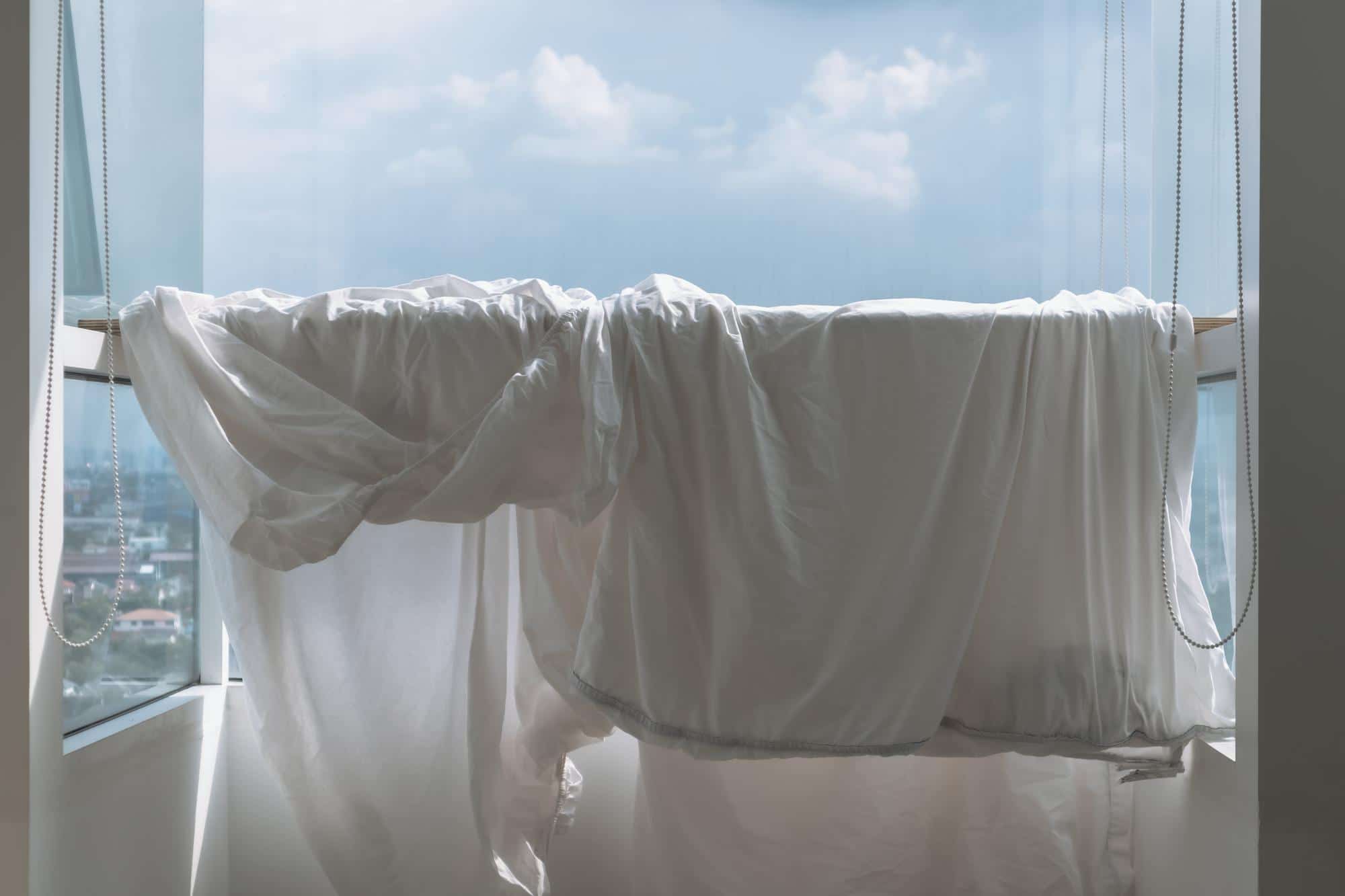 Drap humide suspendu devant une fenêtre ouverte pour aider à rafraîchir naturellement l’air intérieur pendant une période de forte chaleur.