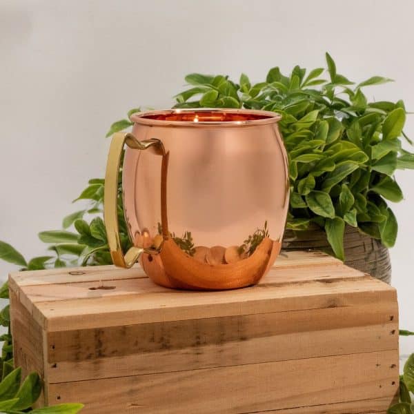 Mug en cuivre brillant posé sur une caisse en bois, accessoire raffiné pour boissons chaudes ou fraîches.