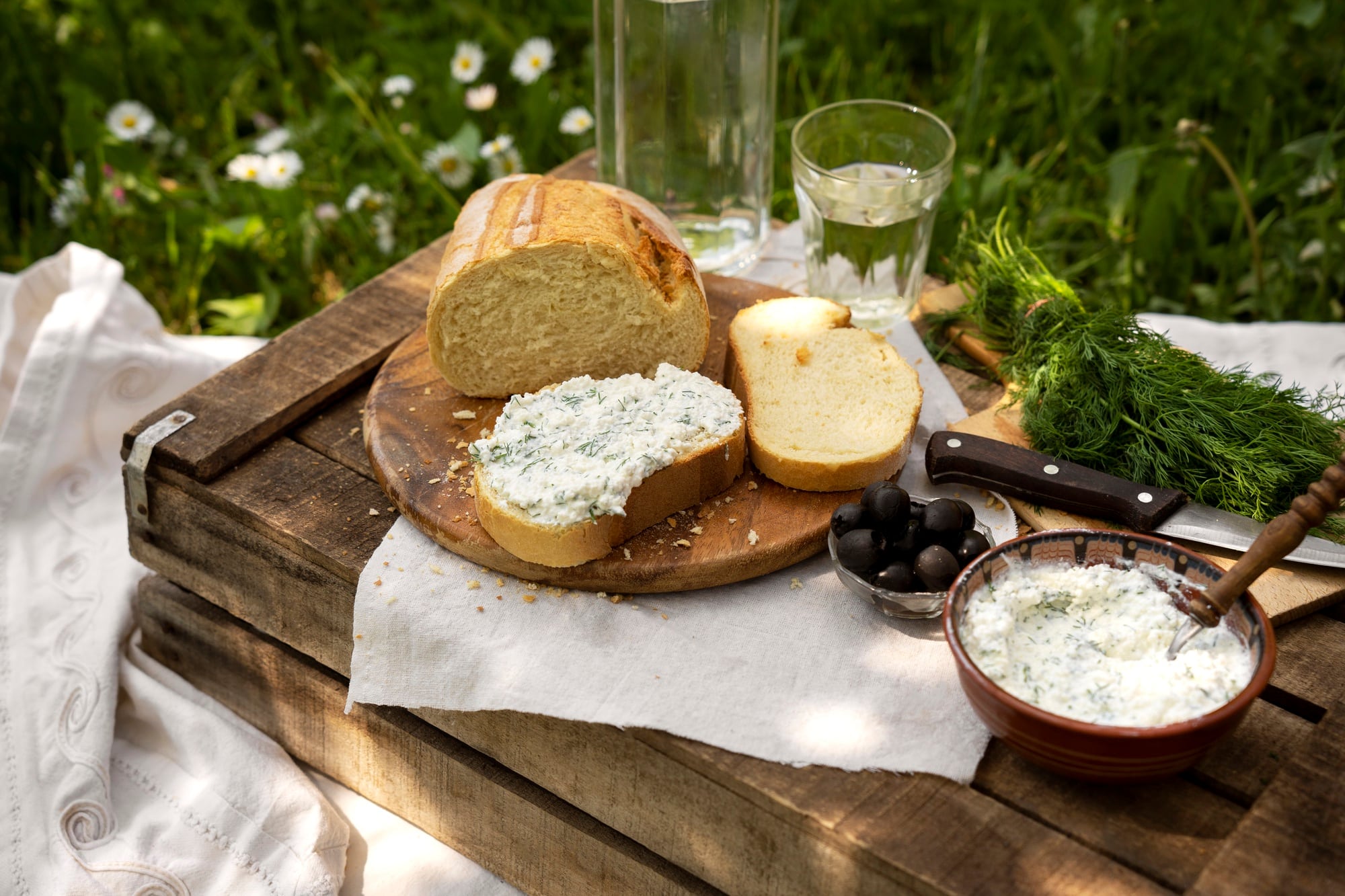 Tartine garnie d'une alternative végétale au fromage frais accompagnée de pain, d'olives et d'herbes fraîches lors d'un pique-nique.