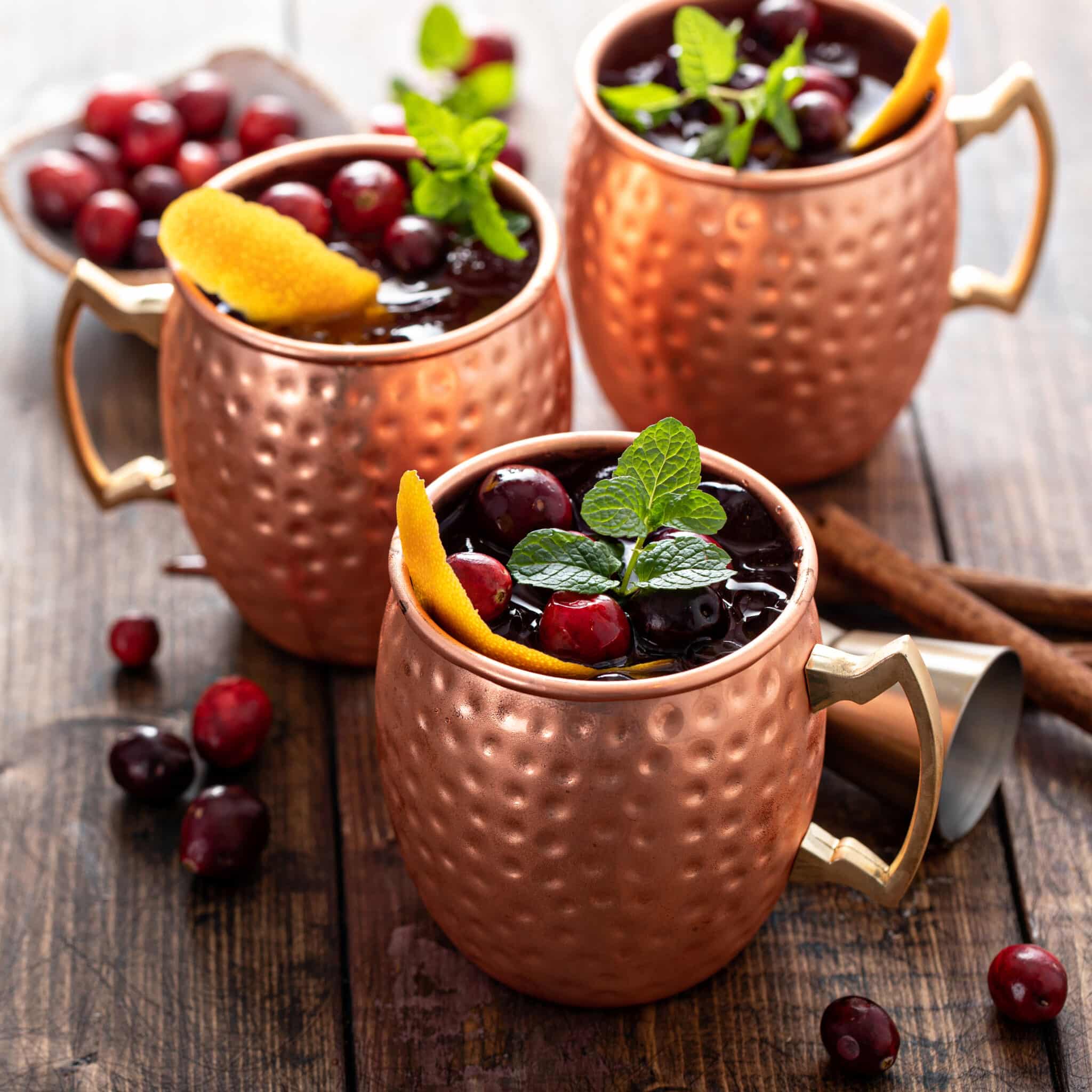 Trois mugs martelés en cuivre contenant une boisson aux fruits rouges, à la menthe et aux agrumes.