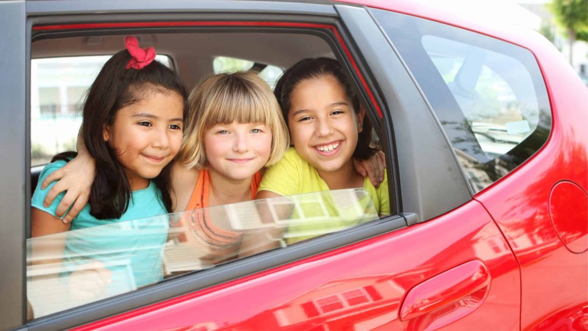 Trois enfants souriants assis à l’arrière d’une voiture, illustration du covoiturage pour accompagner les enfants à leurs activités extrascolaires.