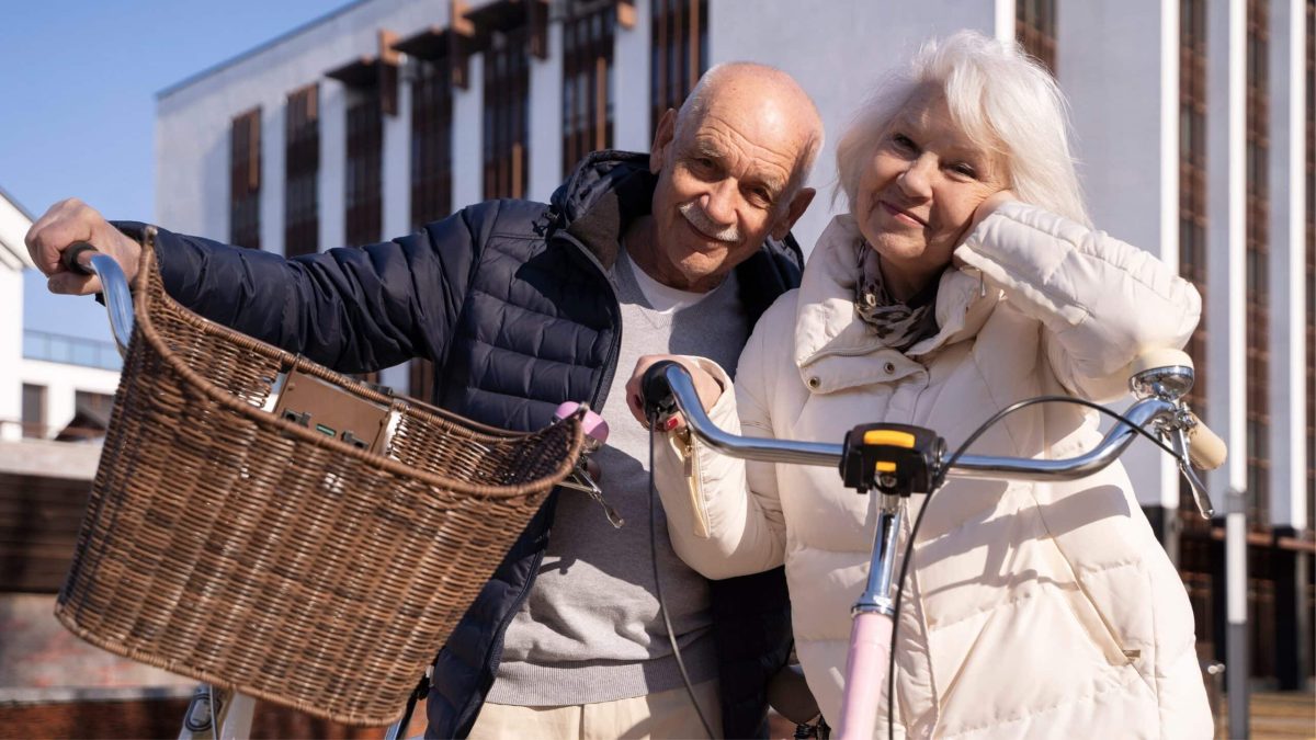 Couple de seniors souriants tenant leurs vélos en centre-ville, symbole d’un mode de vie actif et écologique à tout âge.