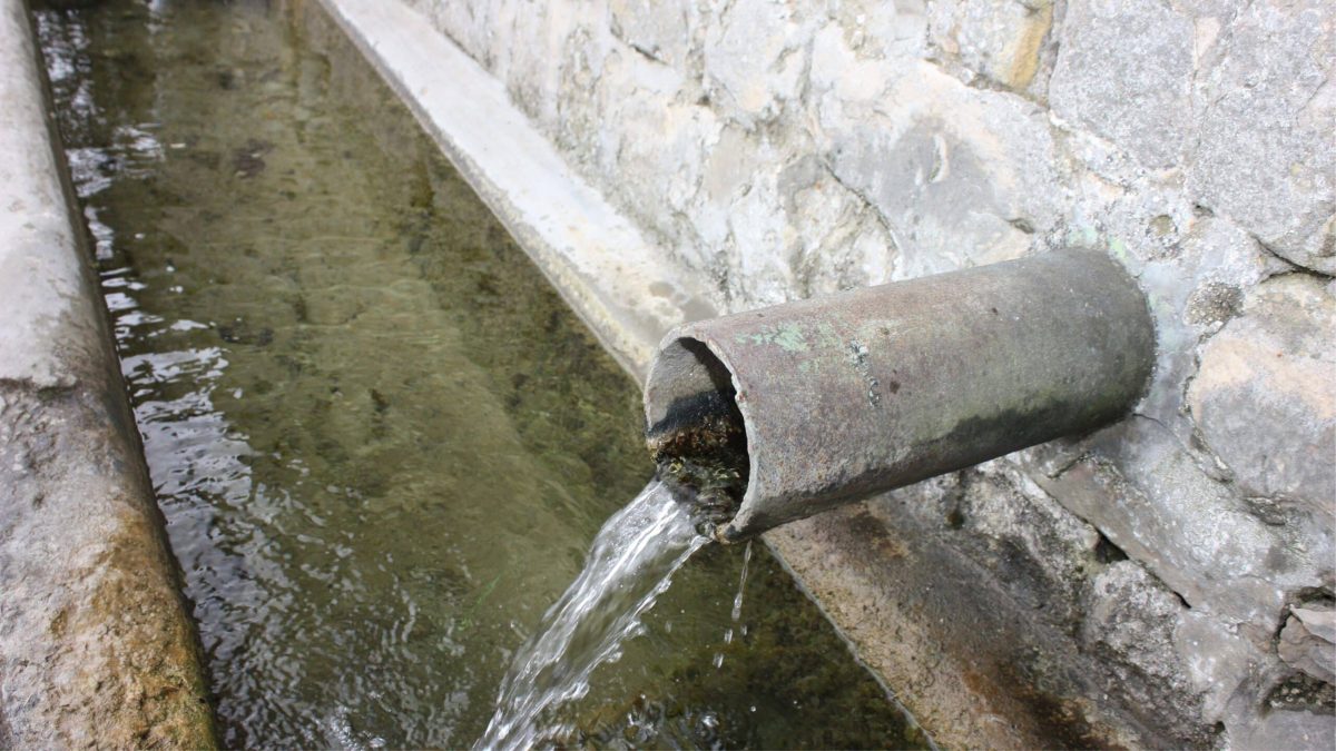 Canal d’eau claire sortant d’un tuyau ancien, illustrant la contamination de l’eau potable par les pesticides et son coût pour les particuliers