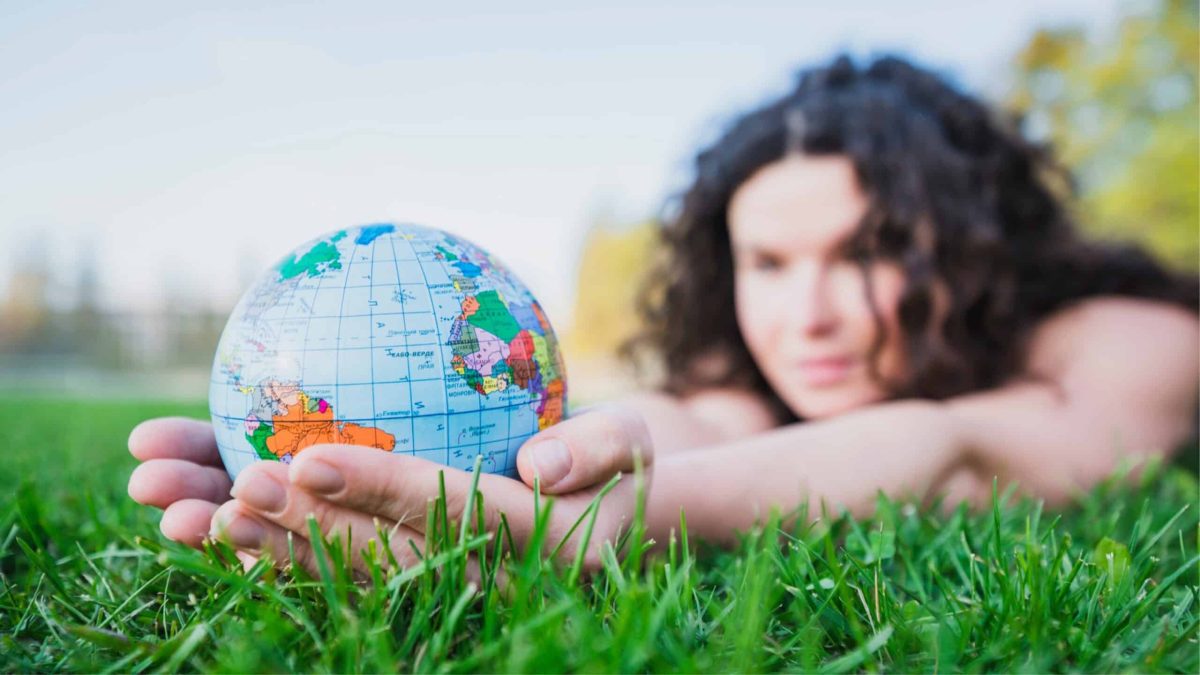 Femme allongée dans l’herbe tenant un globe terrestre dans ses mains, symbole d’une vision globale du bio et de l’écologie.