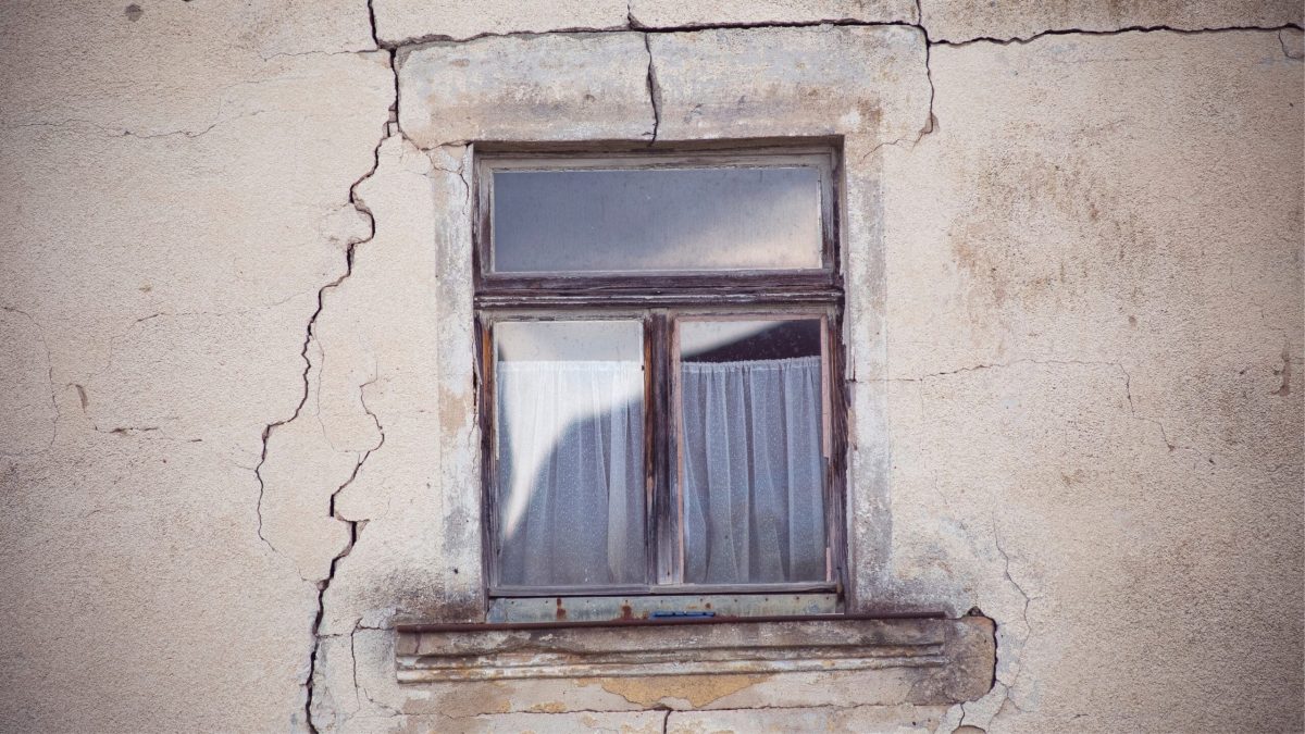 Façade de maison ancienne avec fissures visibles autour d’une fenêtre, illustration des dégâts causés par le retrait-gonflement des sols argileux.