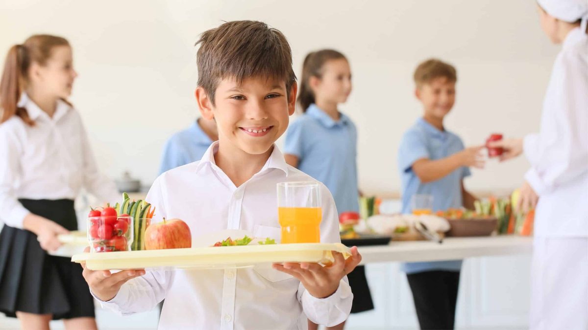 Enfant souriant avec un plateau repas bio dans une cantine scolaire, illustrant la transition vers plus de bio et moins de déchets.