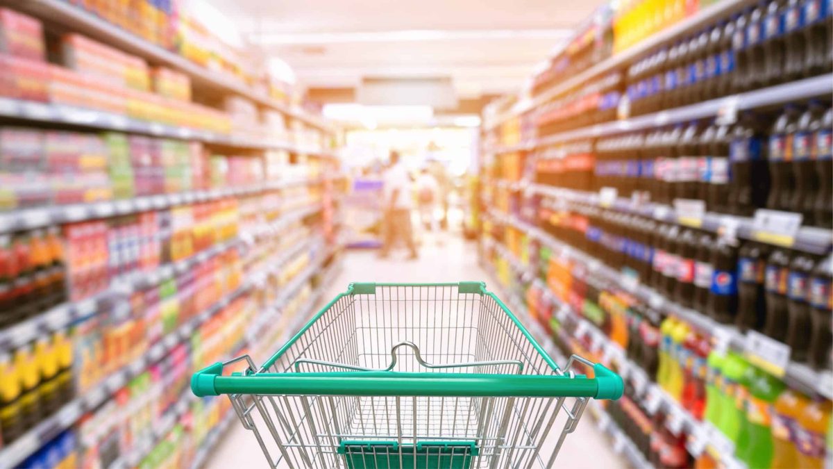 Chariot de supermarché dans un rayon rempli de produits alimentaires ultra-transformés.